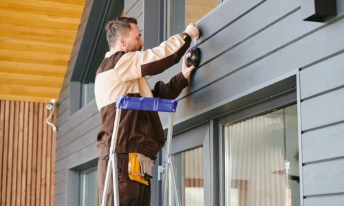 Young man in uniform holding alarm system while standing on ladder