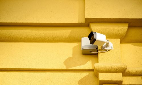 close up view of security camera on yellow building facade