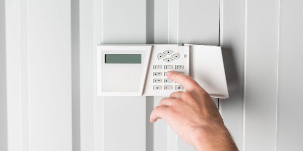 person typing password on home security alarm, security system concept