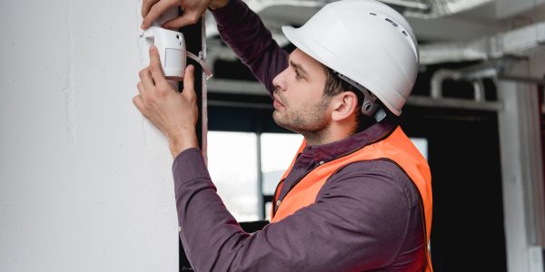 serious firefighter in uniform and helmet checking fire alarm