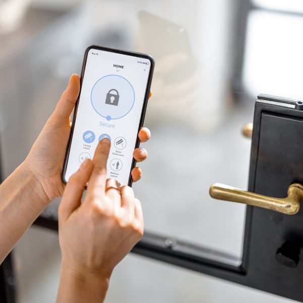 Smartphone with launched application for alarm security system, lock or unlock entrance door on interior background. Focus on mobile. Smart and safe home concept.