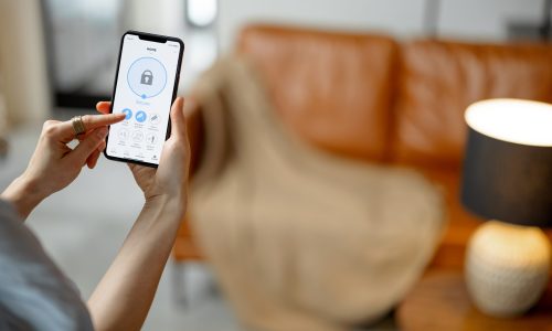 Smartphone with launched application for alarm security system, lock or unlock entrance door on interior background. Focus on mobile. Smart and safe home concept.