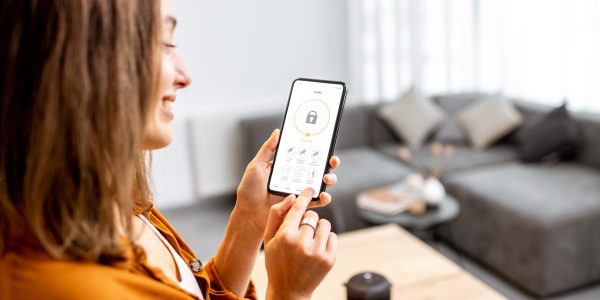 Young woman holding smart phone with launched security application at home. Concept of controlling and managing home security from a mobile device